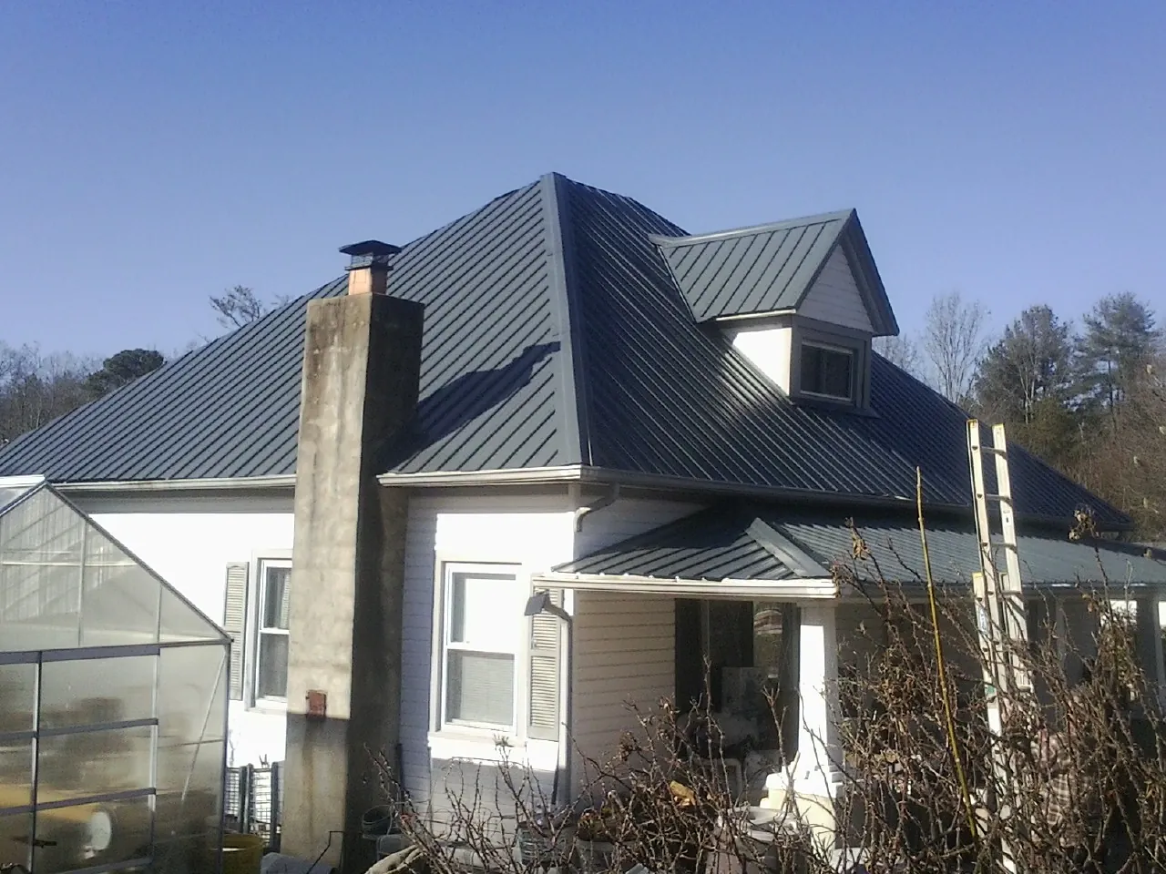 Dark blue standing seam metal roof on a white farmhouse with dormer — Slate & Tile Roof Repair by Roofing Brothers in Scipio Center
