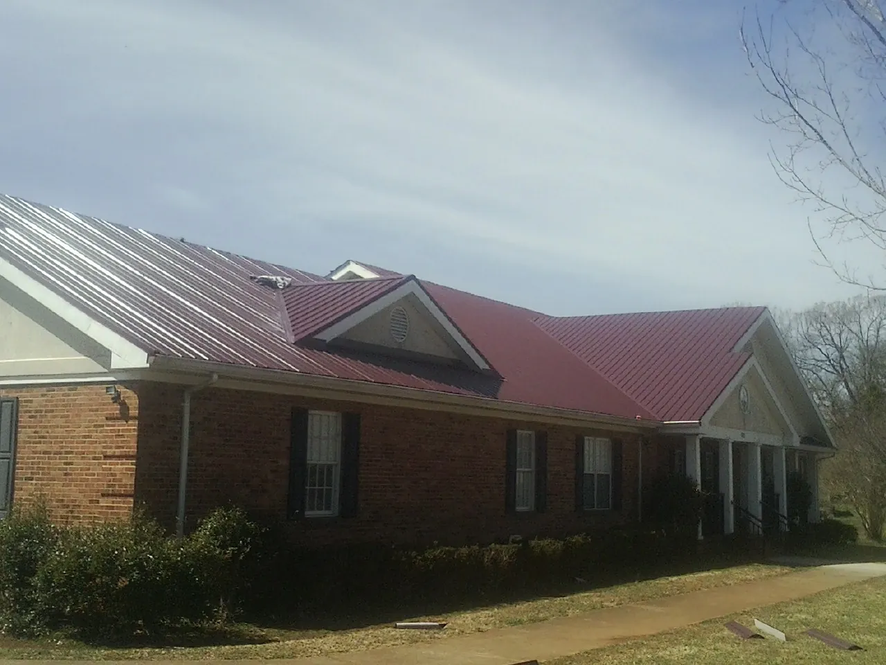 Red metal roof with gabled entries on a long brick building, from a Hail Damage Roof Repair job in Scipio Center