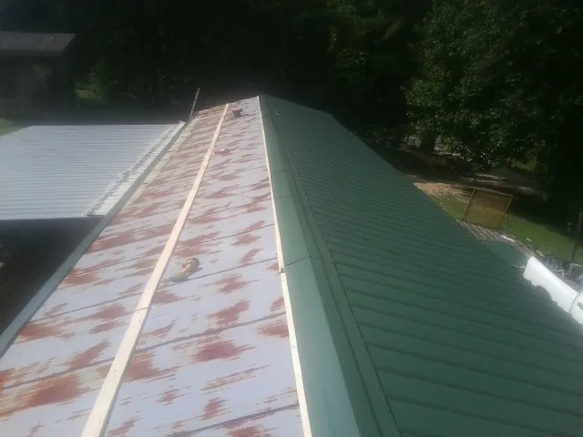 Old rusted panels beside newly installed green metal roofing — Wind Damage Roof Repair by Roofing Brothers in Scipio Center