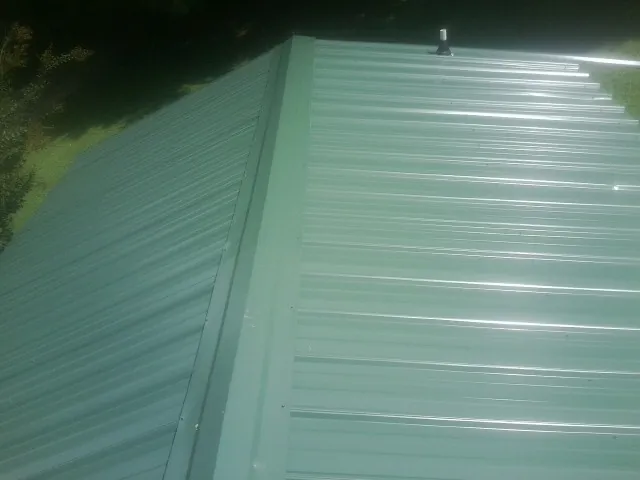 New green metal panels meeting at the ridge of a roof — Flat Roof Repair work by our crew in Scipio Center