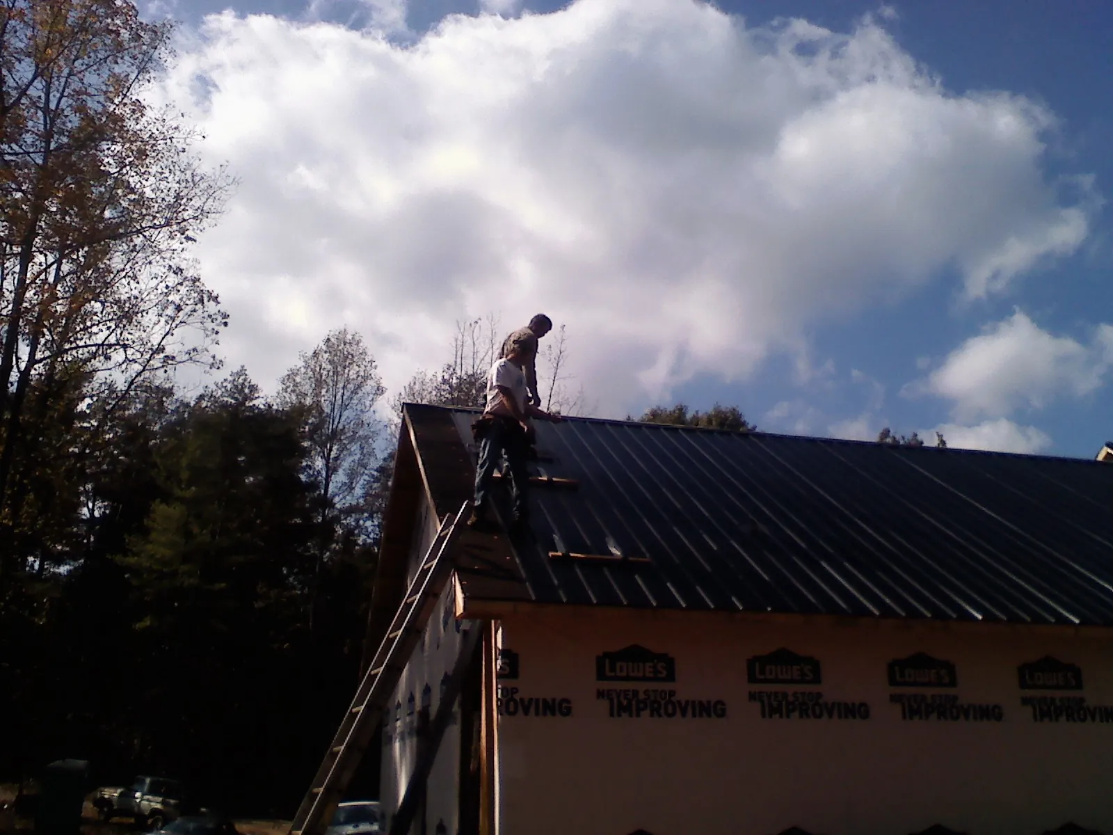 Roofer fastening dark metal panels high against a cloudy sky, from a Roof Inspection job in Scipio Center