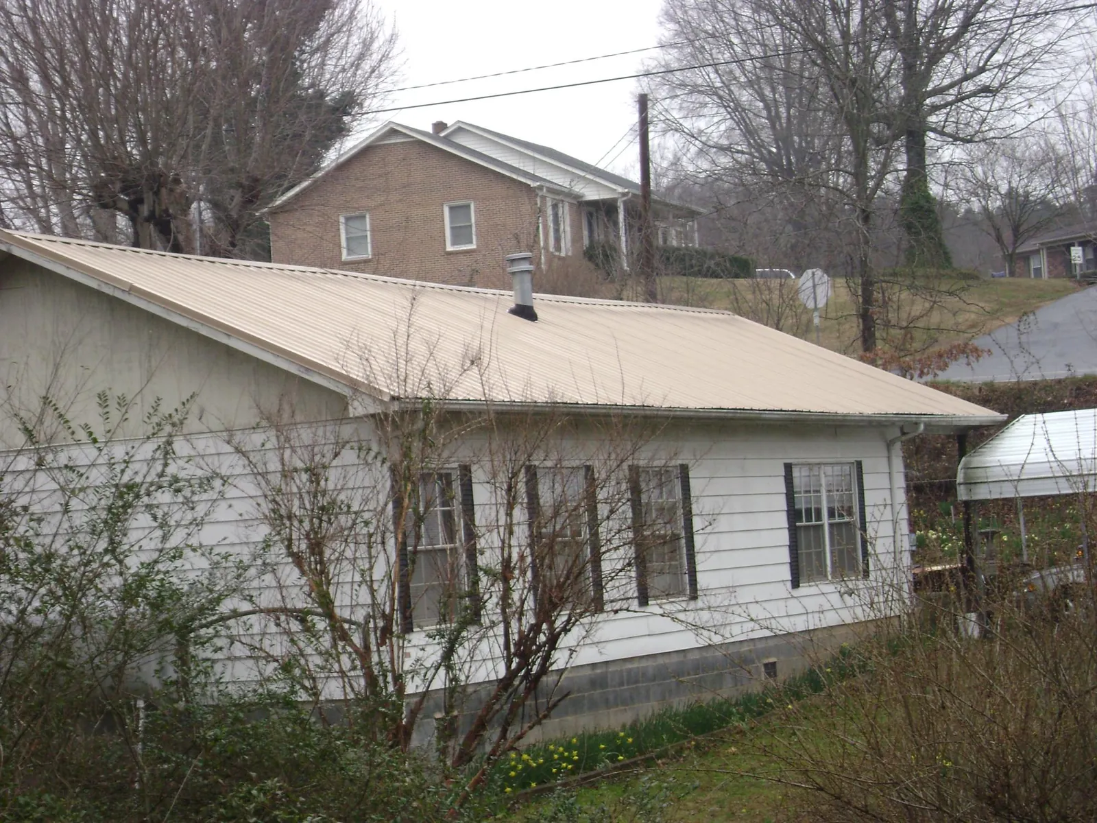 Tan metal roof on a white sided house set into a hillside — Commercial Roofing by Roofing Brothers in Scipio Center
