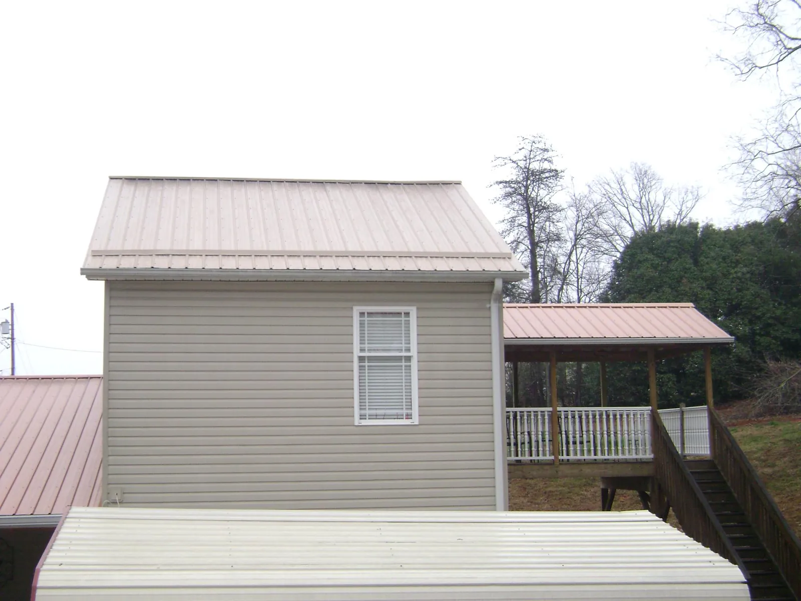 Tan metal roofs on a two story addition and attached porch, from a Roof Replacement job in Scipio Center