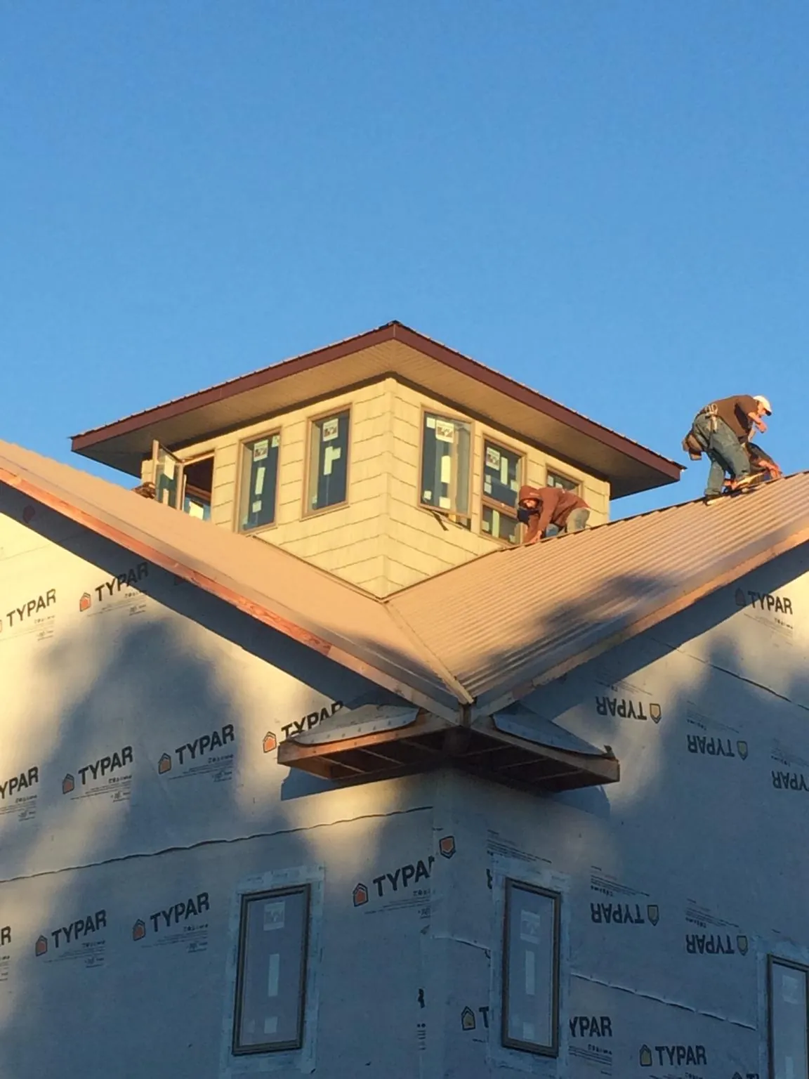 Roofers working around a rooftop cupola on a new metal roof at sunset — Roof Waterproofing in Scipio Center by Roofing Brothers